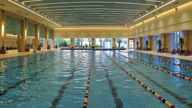 A large indoor swimming pool with multiple lanes, surrounded by lounge areas and large windows. - Quanzhou Guest House Hotel (Quanzhou)