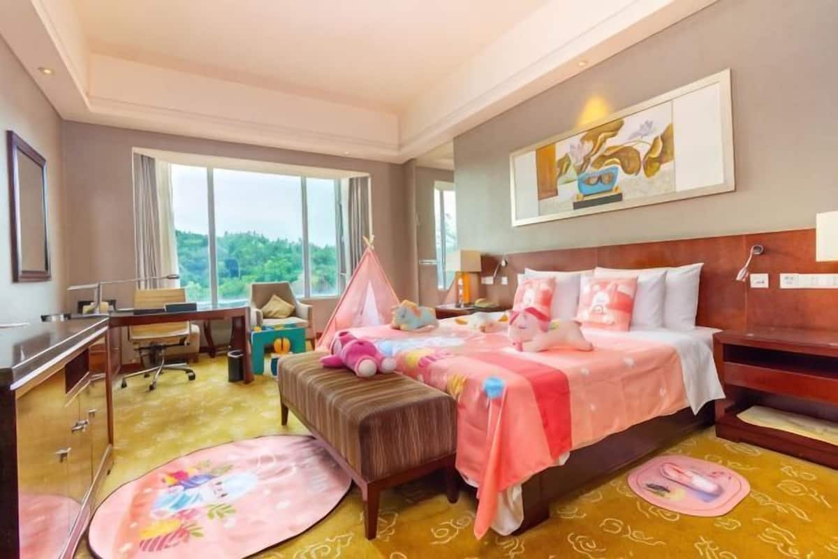 Een hotelkamer met een bed, bureau, stoel en grote ramen.