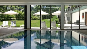 An indoor swimming pool with clear glass walls, lounge chairs, and umbrellas. - Brugger´s Genießerhotel Lanersbacherhof (Tux)