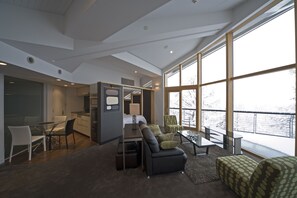 Une chambre d’hôtel moderne dotée d’une cuisine, d’un coin repas et de grandes fenêtres donnant sur un paysage enneigé.