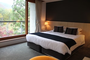 A hotel room with a large bed, a bedside table with a lamp, and a view of trees through a window. - The Ridge Hotel & Apartments (Hakuba)