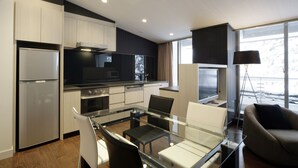 A modern kitchen with a dining area, including a glass table and chairs, and a sofa. - The Ridge Hotel & Apartments (Hakuba)