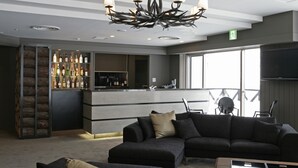 A modern bar area with a counter and shelves of bottles, a large sectional sofa, and a chandelier. - The Ridge Hotel & Apartments (Hakuba)
