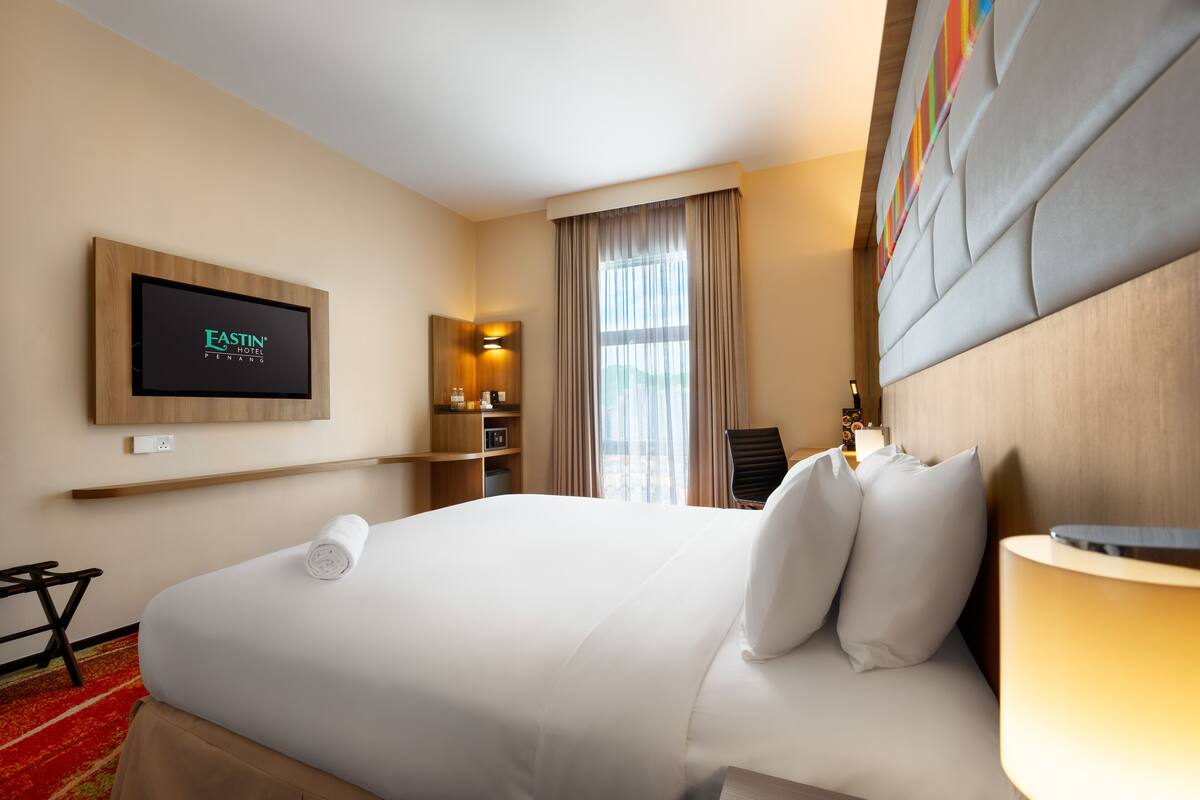 Ein Hotelzimmer mit einem großen Bett, einem an der Wand montierten Fernseher, einem Schreibtisch und einem Stuhl.