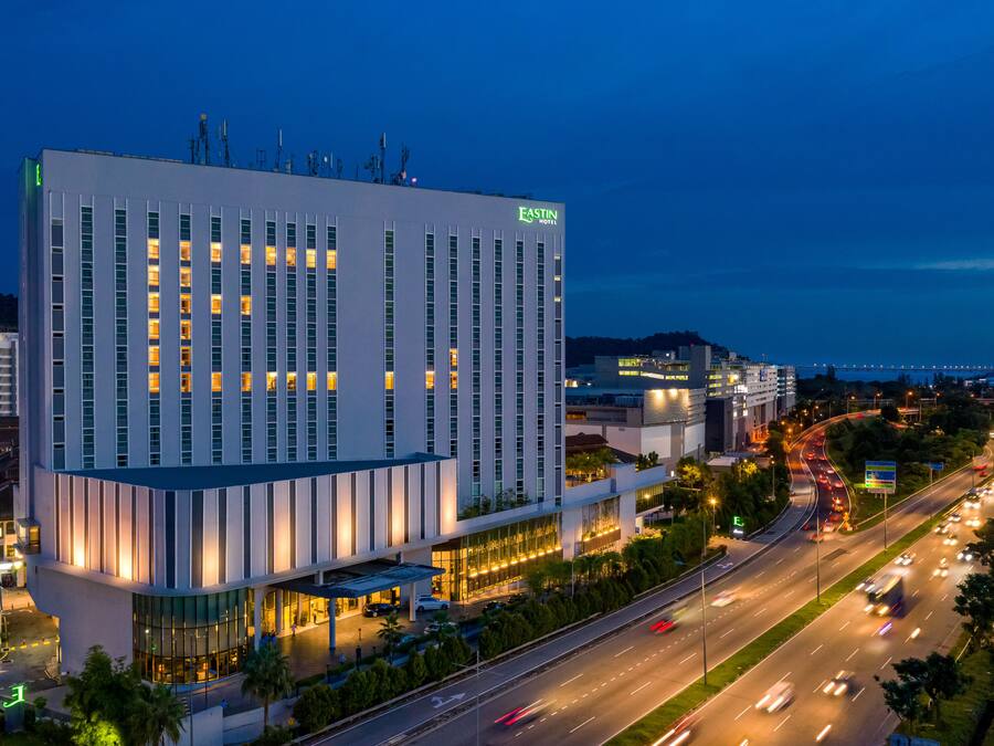 A modern hotel with a prominent 'EASTIN HOTEL' sign, featuring a large glass facade and a well-lit entrance.