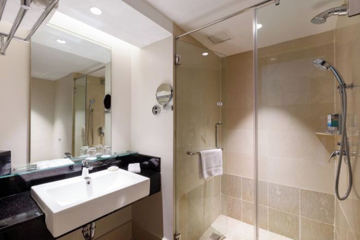 Un baño moderno con ducha de vidrio, lavamanos blanco y un espejo grande.