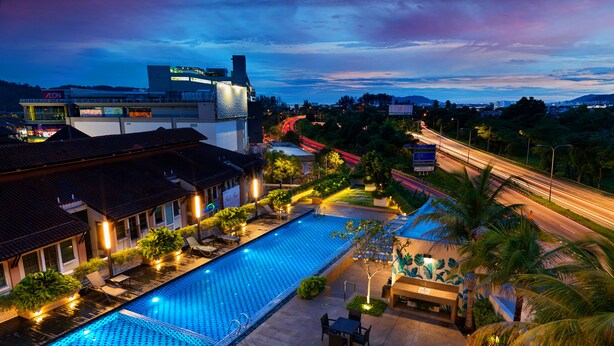 A swimming pool with lounge chairs and tables, surrounded by greenery and a building with a sign. - Eastin Hotel Penang (George Town)
