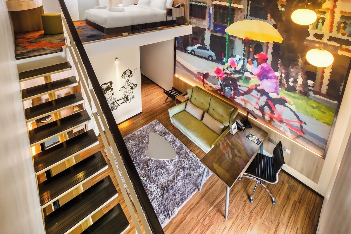 Ein Mehrstöckiges Hotelzimmer mit Treppe, Sofa, Schreibtisch und einem großen abstrakten Gemälde.