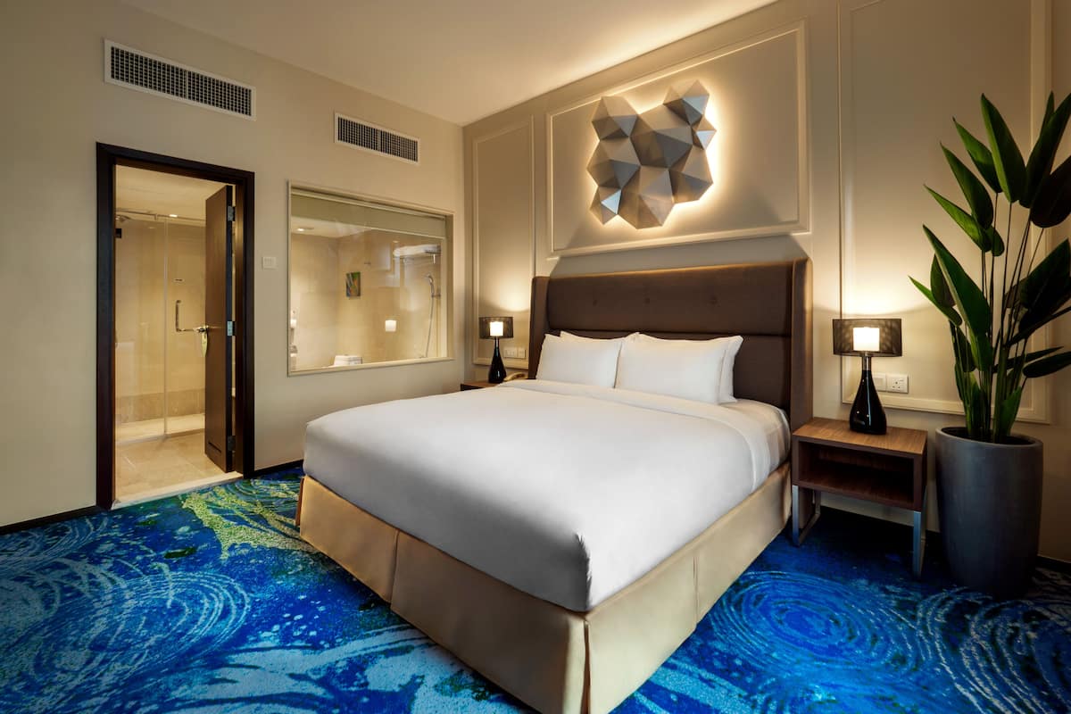 Ein Hotelzimmer mit einem großen Bett, einem Spiegel, einem Nachttisch mit Lampe und einer Zimmerpflanze.