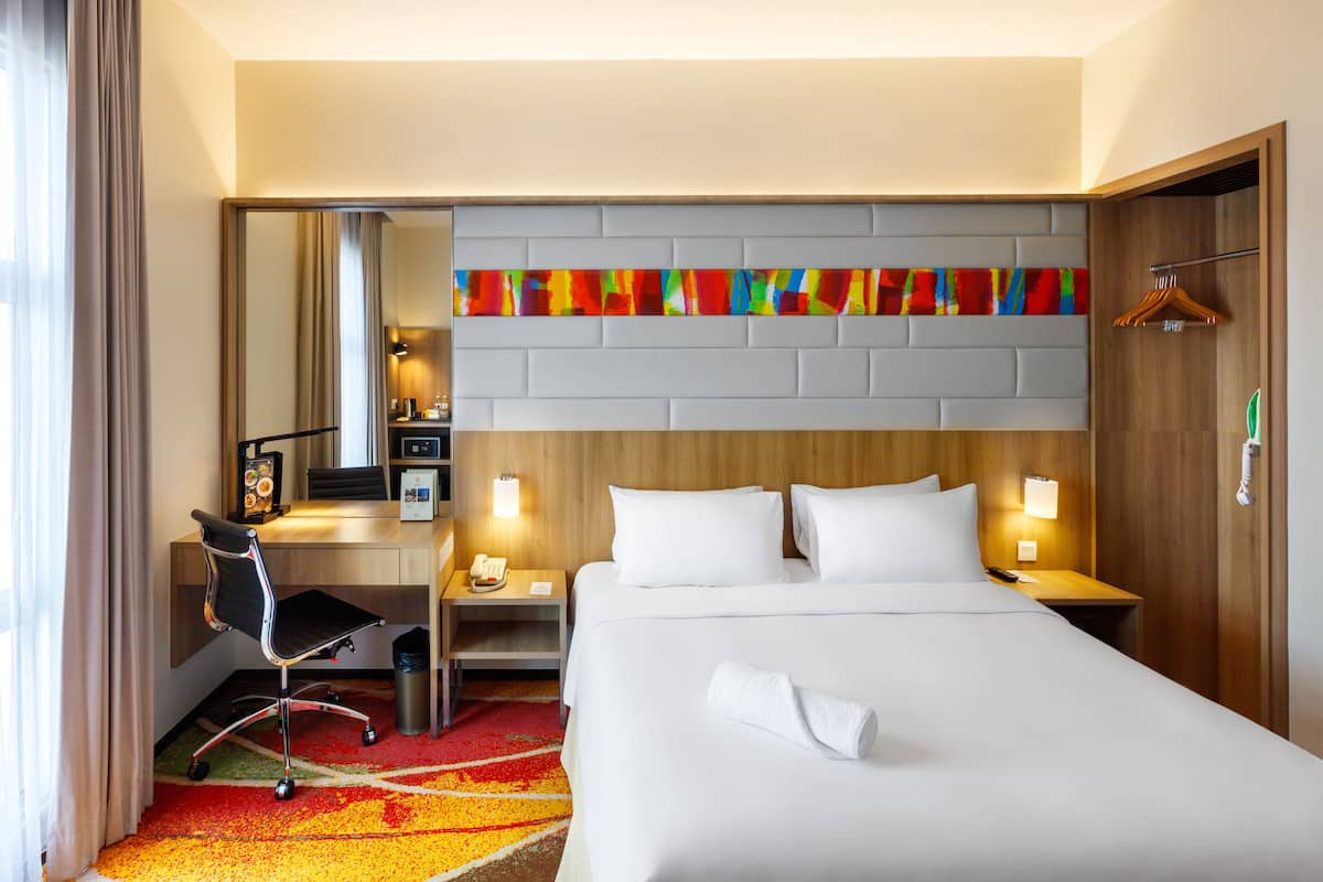 Ein Hotelzimmer mit Bett, Schreibtisch, Stuhl und einem farbenfrohen, abstrakten Kunstwerk an der Wand.