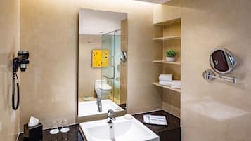 A modern bathroom with a large mirror, a white sink, a handheld showerhead, and a glass-enclosed shower.