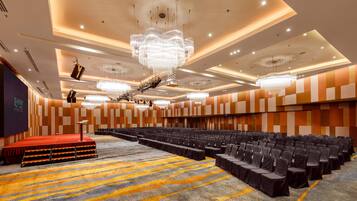 Une grande salle de conférence avec de nombreuses rangées de chaises, une scène recouverte d’un tapis rouge et de nombreux lustres.