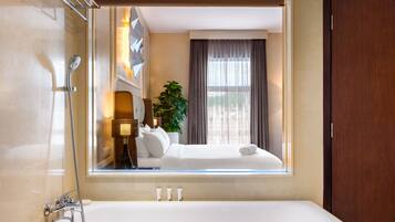 A hotel bathroom with a large mirror, a bathtub, a shower, and a window with curtains.