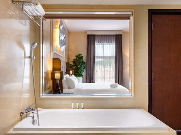 Un baño de hotel con un espejo grande, una bañera, una ducha y una ventana con cortinas.