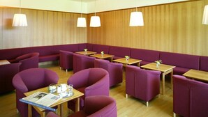 A restaurant with purple seating, wooden tables, and pendant lights. - St. Virgil (SALZBURG)