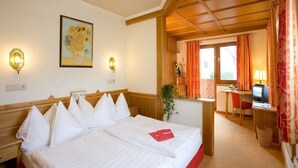 A hotel room with a large bed, a desk with a computer, a television, and a small table with a plant. - St. Virgil (SALZBURG)