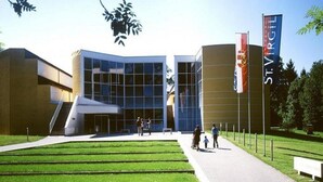 A modern building with a glass facade, a staircase leading to the entrance, and a flagpole with a flag. - St. Virgil (SALZBURG)