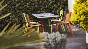 Eine Terrasse mit Tisch und Stühlen, umgeben von einer Hecke.