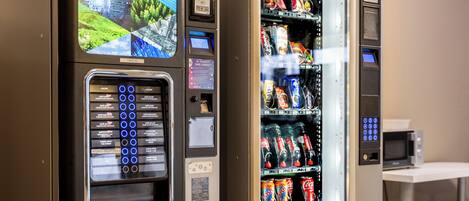 Máquina expendedora con variedad de aperitivos y bebidas, una interfaz de pago y una pantalla digital.
