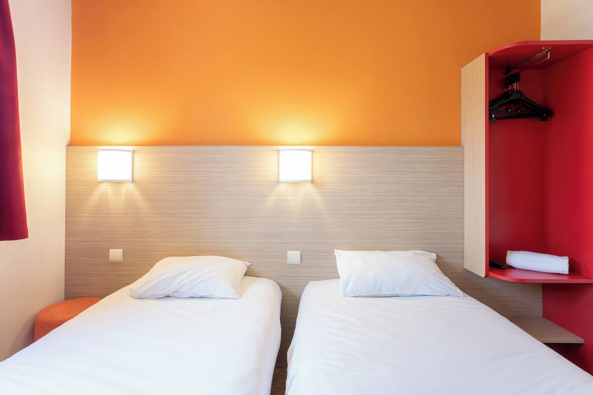 Een hotelkamer met twee éénpersoonsbedden, een rode garderobe en twee wandlampen.
