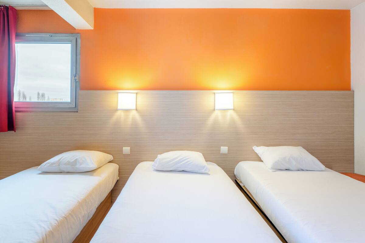 Een hotelkamer met twee enkele bedden, een houten hoofdbord en twee wandlampen.