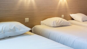 Ein Hotelzimmer mit zwei Betten, jeweils mit weißer Bettwäsche und Kissen. Zwei Wandleuchten sind am Kopfteil angebracht.