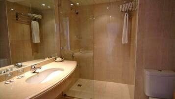 Une salle de bain moderne avec un grand miroir, un lavabo et une douche séparée par une paroi de verre.