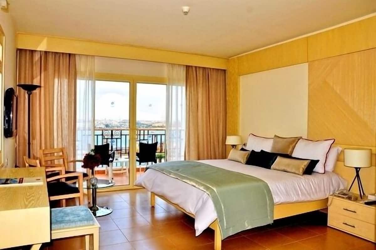 A hotel room with a bed, a desk, a chair, and a balcony with a view.