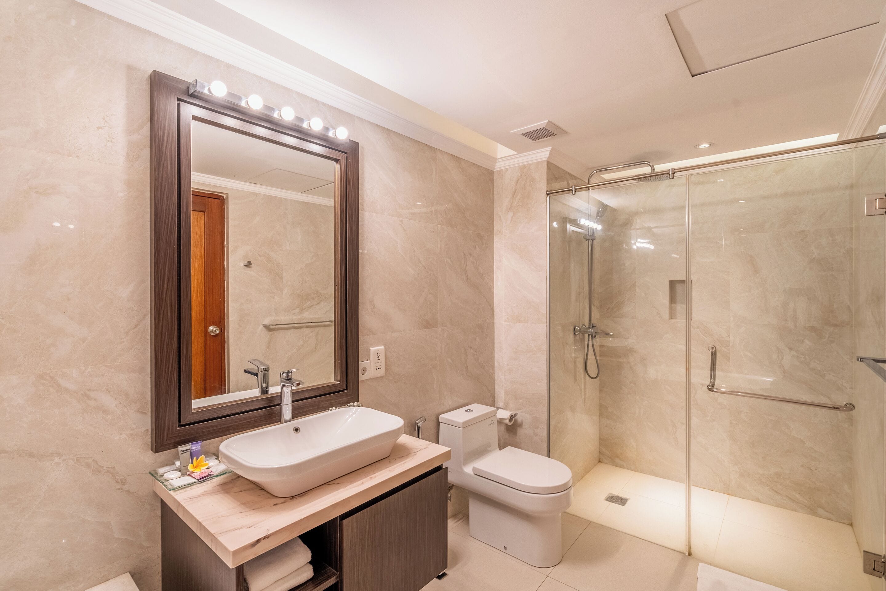 A modern bathroom with a large mirror, a sink, a toilet, and a glass-enclosed shower.