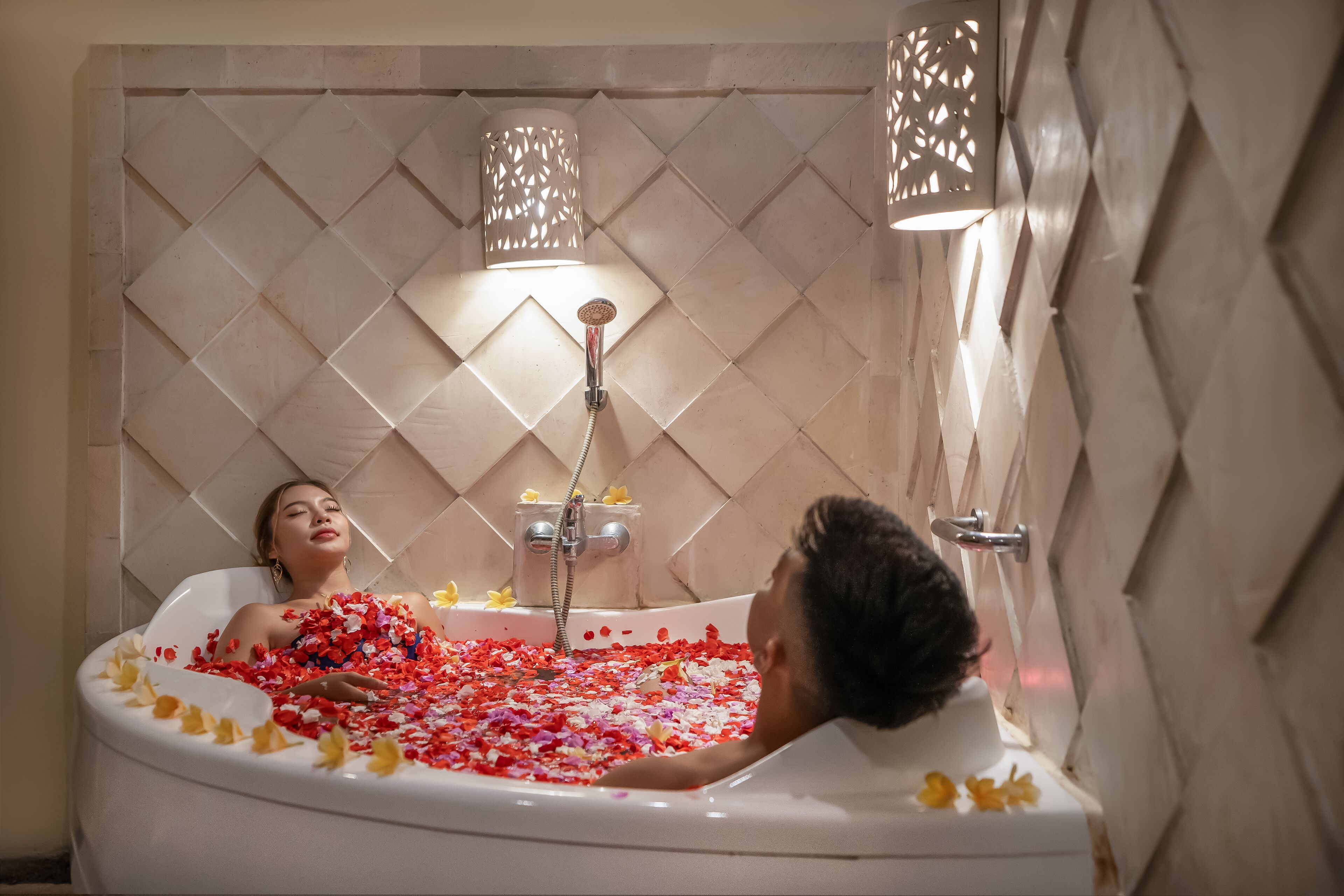 A bathtub filled with rose petals and a showerhead above.