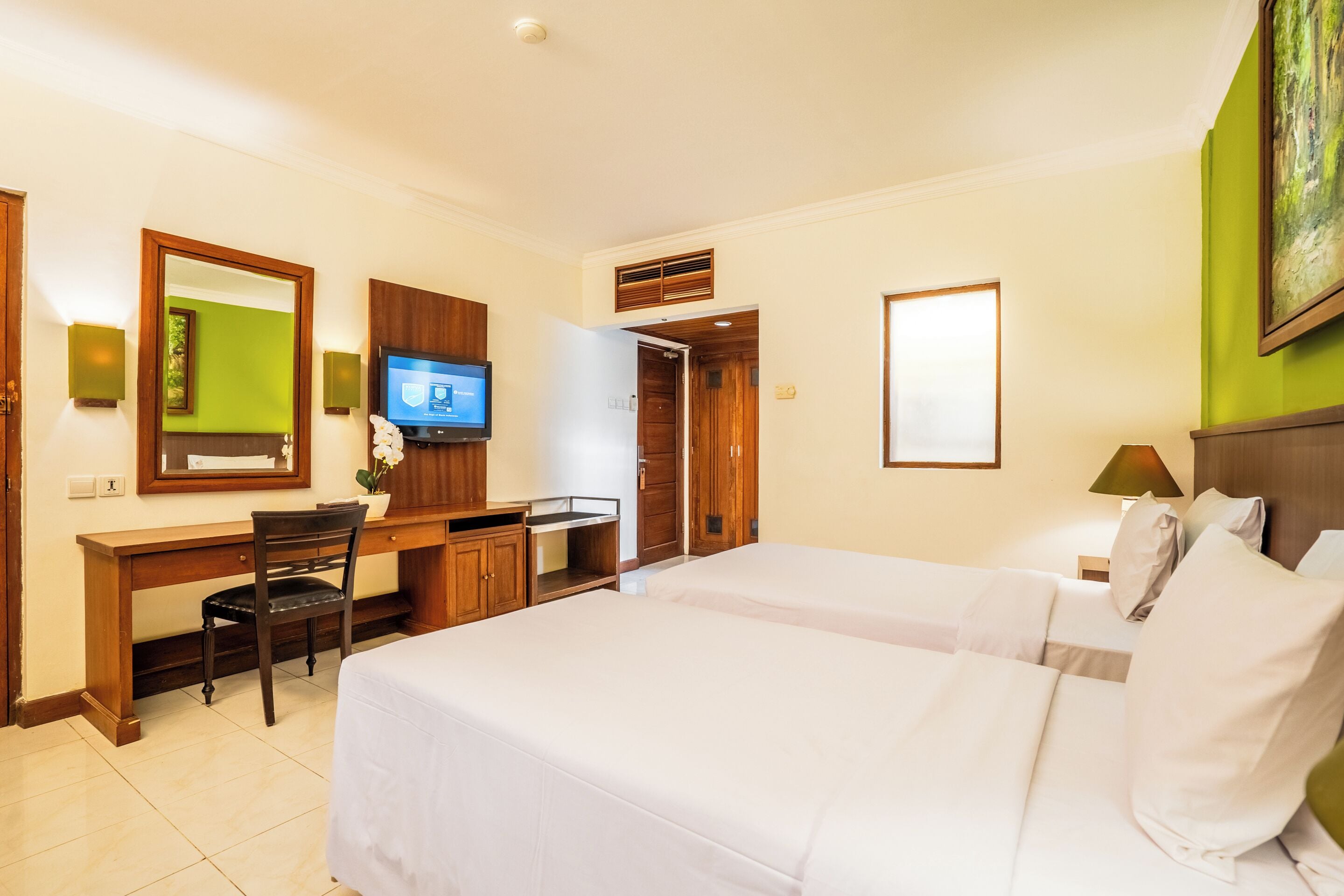 A hotel room with a bed, a desk, a chair, a television, and a painting on the wall.
