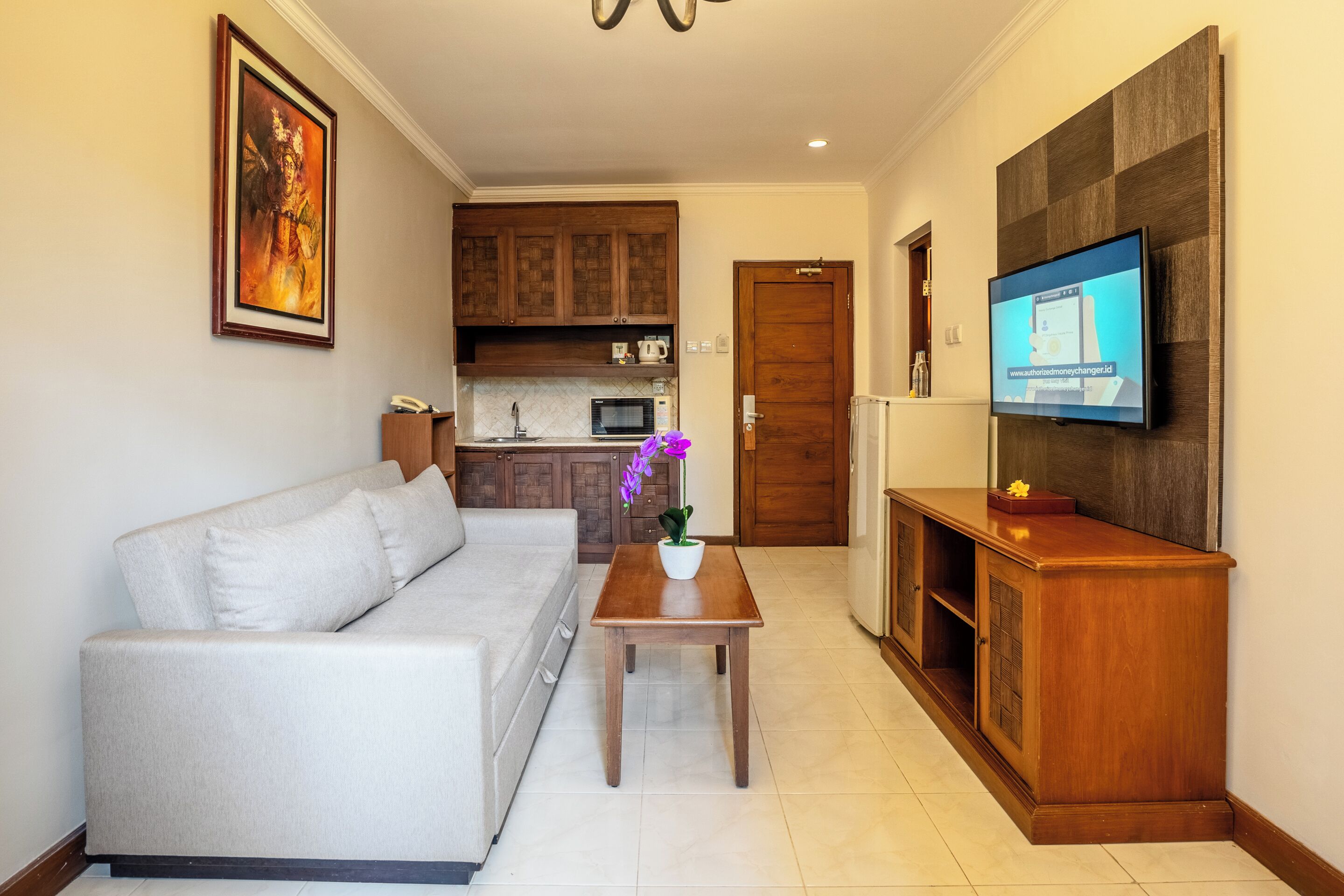 A living room with a sofa, a coffee table with a flower vase, a TV on a wooden stand, and a kitchen in the background.