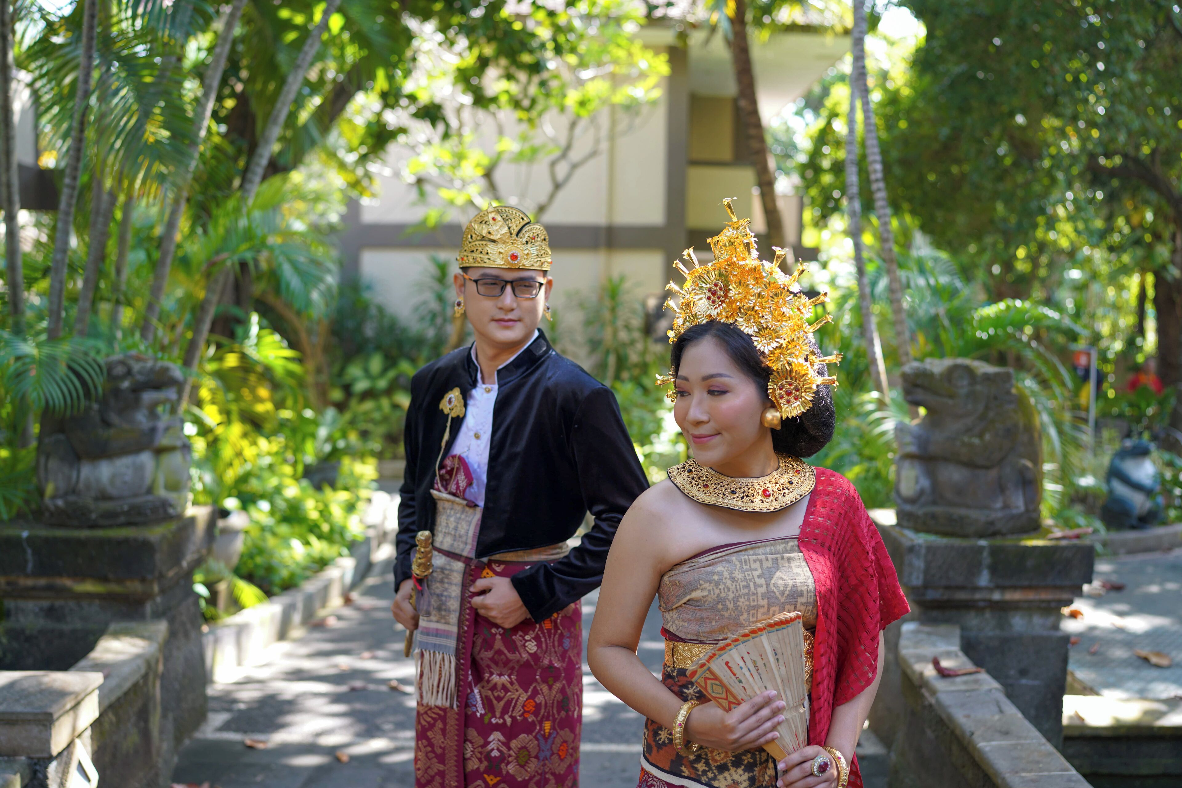 A couple in traditional attire standing on a stone pathway surrounded by greenery.
