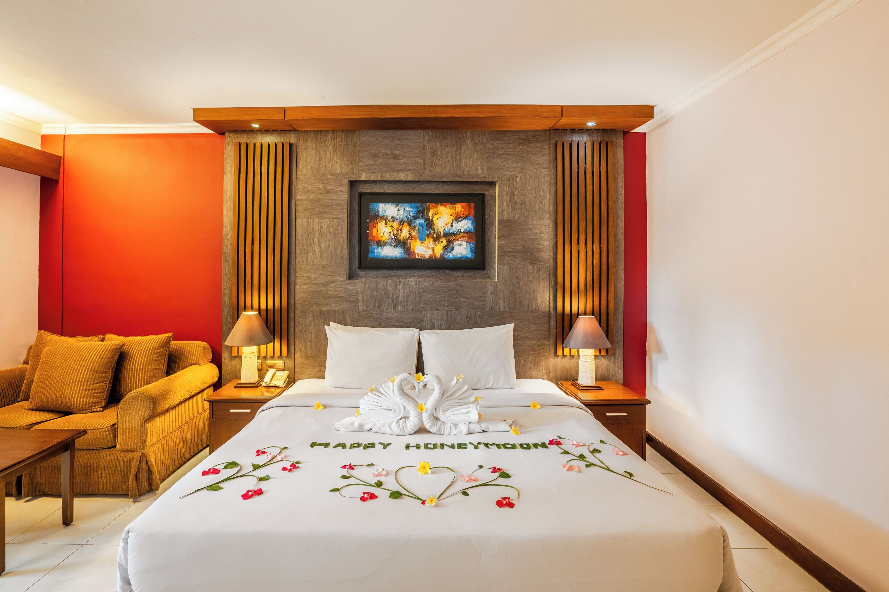 A hotel room with a bed, a sofa, two nightstands, and a painting on the wall.