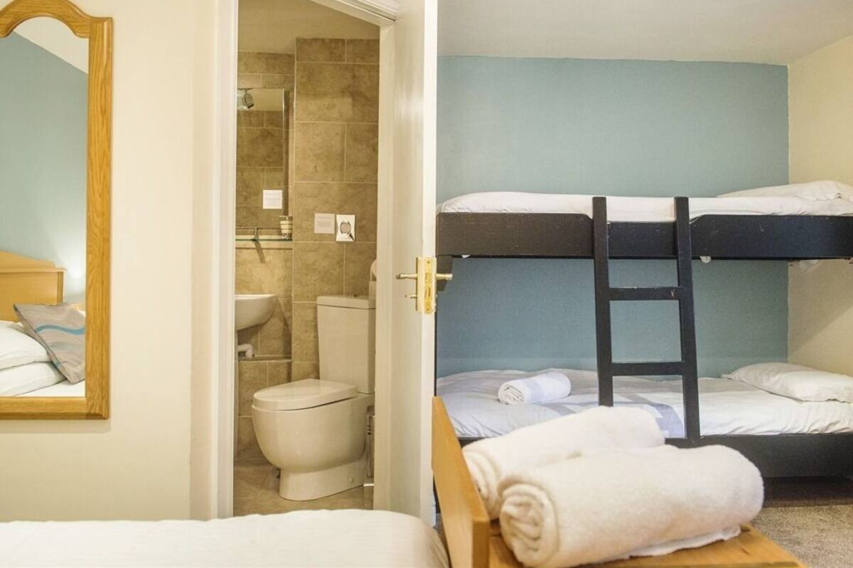 A room with bunk beds, a bathroom with a toilet and sink, and a mirror.