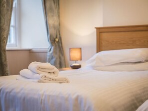 A neatly made bed with white linens and a stack of folded towels on the side. - The Wellington Hotel (Penzance)