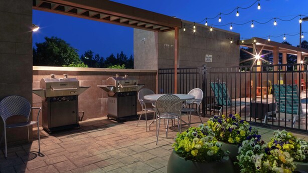 An outdoor patio with a grill, chairs, and potted plants.