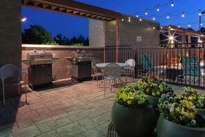 An outdoor patio with a grill, chairs, and potted plants.