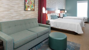 A hotel room with a sofa, two beds, a round ottoman, a large window, and a colorful abstract painting on the wall.