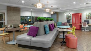 A modern lounge area with a grey sofa, colorful cushions, a small round table, and a red cabinet.