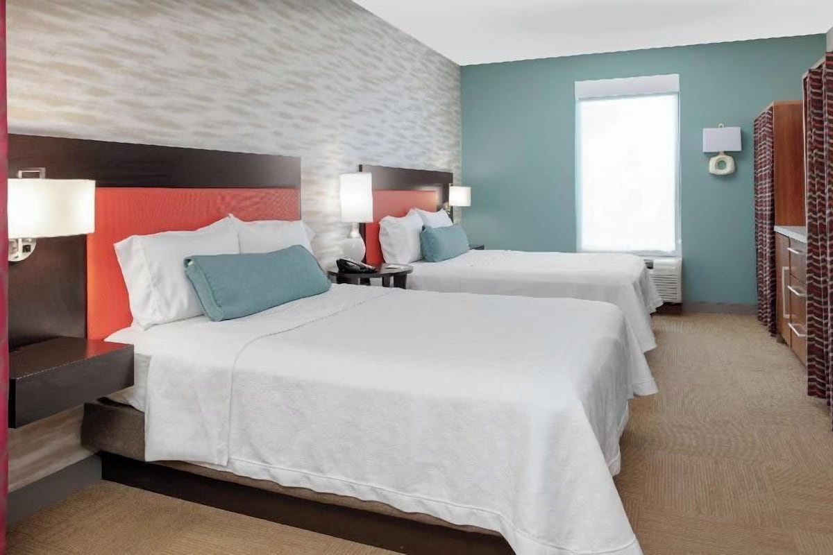 Une chambre d’hôtel avec deux lits, un mur d’accent rouge et une fenêtre avec des rideaux.