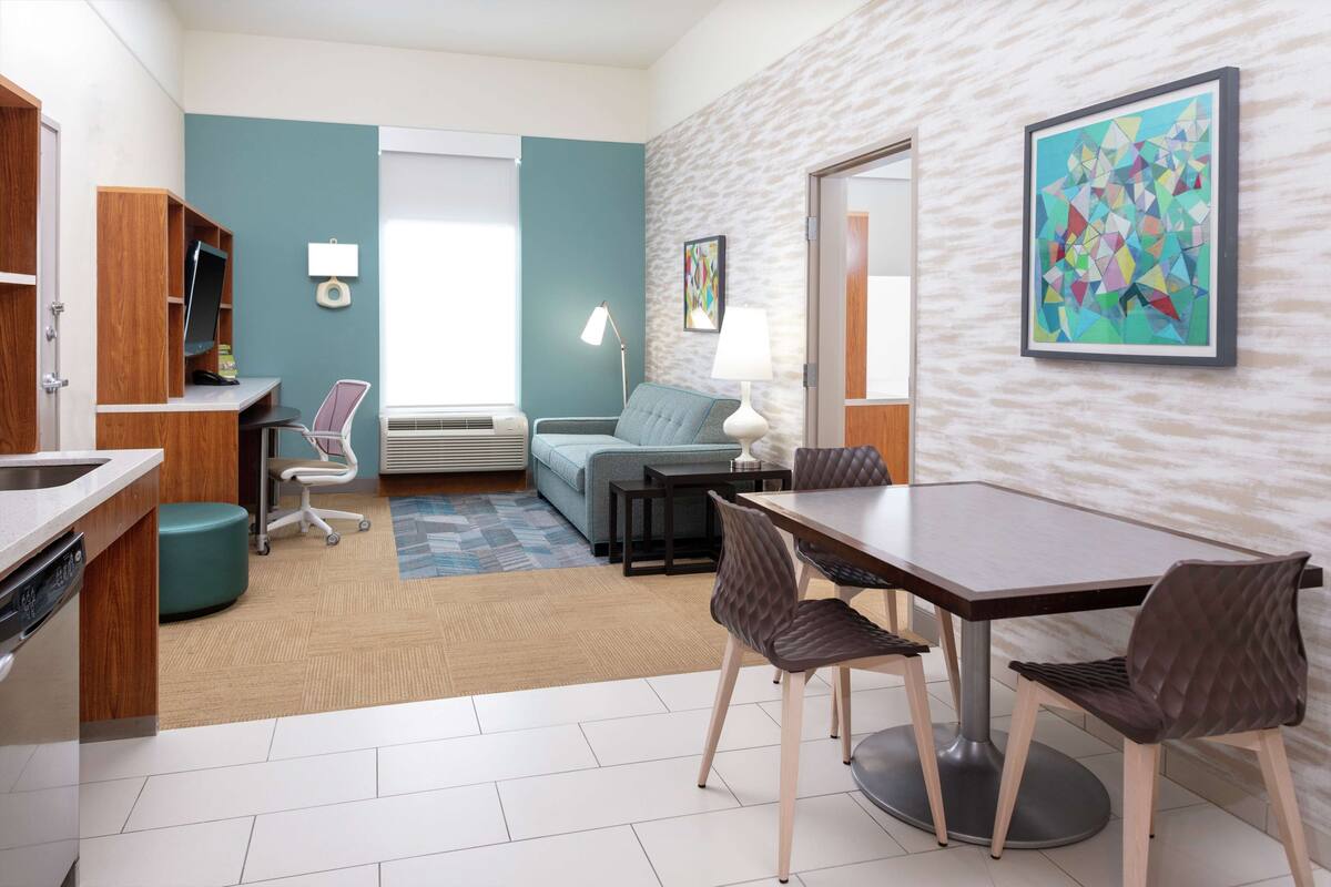 Ein modernes Hotelzimmer mit Küchenzeile, Essbereich, einer Couch und einem großen abstrakten Gemälde.
