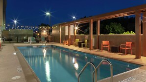 A swimming pool with a pergola, chairs, and a sign indicating a 5ft depth.