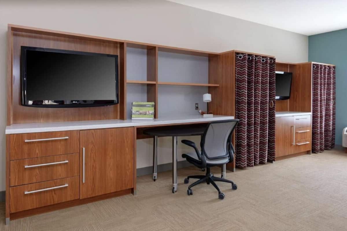 Ein Hotelzimmer mit einem Holztisch, einem Fernseher, einem Sessel und einem Kleiderschrank.