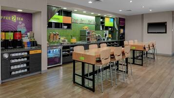 A modern cafe with a coffee bar, seating area, and a TV screen.