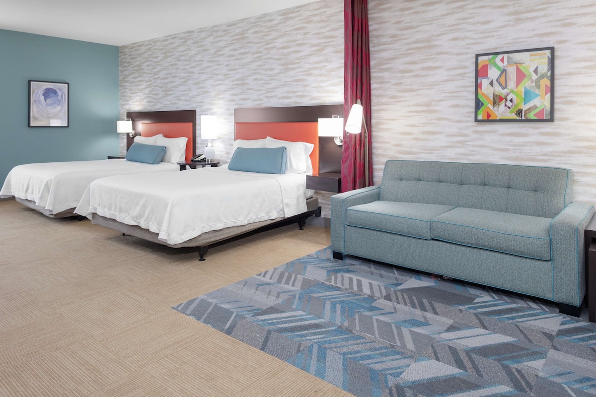Ein Hotelzimmer mit zwei Betten, einem grauen Sofa und einem gemusterten Teppich.