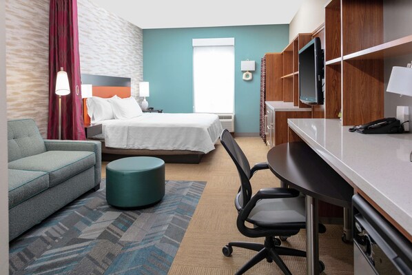 A hotel room with a bed, a desk, a chair, a sofa, and a TV.