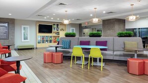 A modern lounge area with a sofa, yellow chairs, red ottomans, and a television on the wall.