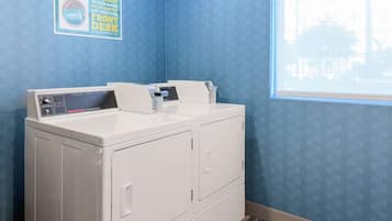 A laundry area with a front-loading washer and dryer, a window with a view of buildings, and a sign on the wall.
