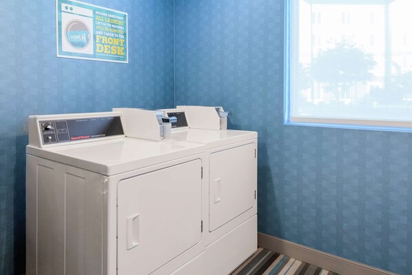 A laundry area with a front-loading washer and dryer, a window with a view of buildings, and a sign on the wall.